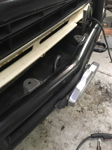1981 Ford Bronco - Close-up of the front bumper and grille area of a 1981 Ford Bronco, showing tow hooks and a light attachment.