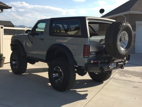 1988 Ford Bronco - This lifted Ford Bronco sits on a paved driveway with a house and fence in the background.