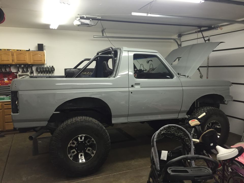 Gray Ford Bronco with roll cage, lifted suspension, and aftermarket wheels in a garage