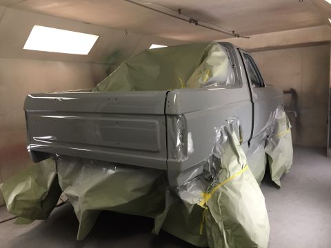 1988 Ford Bronco - A pickup truck is being prepped for painting inside a booth, with protective coverings on its wheels and body panels.