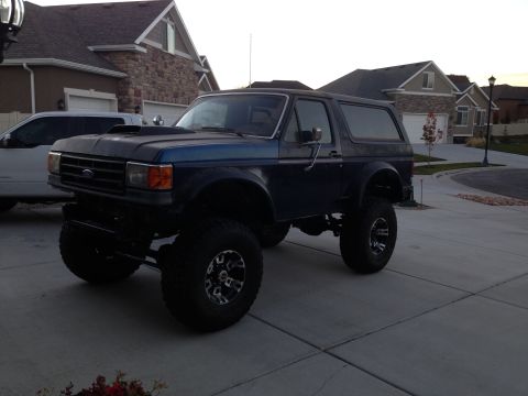 1988 Ford Bronco - This lifted Ford Bronco has an aftermarket hood scoop and is parked in a suburban driveway.
