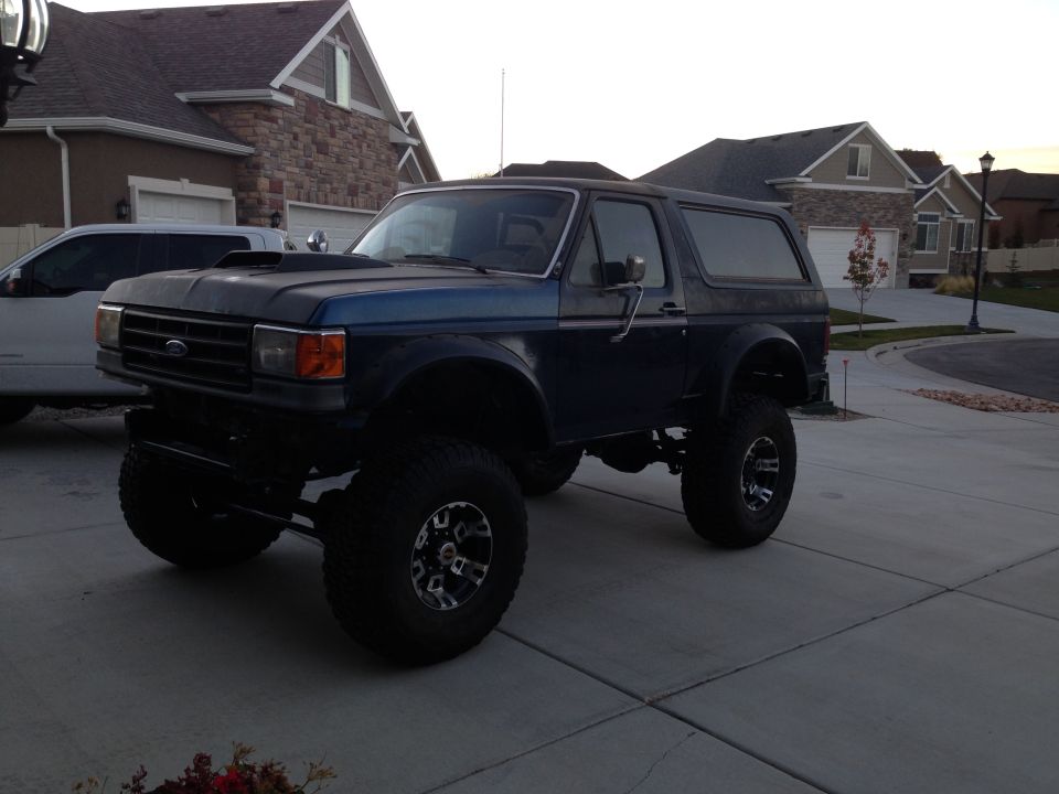 Lifted dark blue Ford Bronco parked on driveway, aftermarket hood scoop
