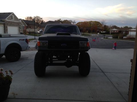 1988 Ford Bronco - A lifted black Ford truck sits in a driveway as a child rides a scooter in the background.