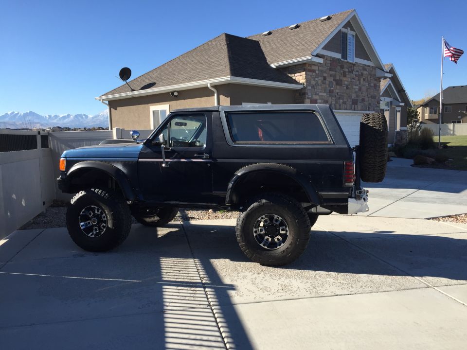Dark blue 1988 Ford Bronco parked in a driveway with a spare tire on the back