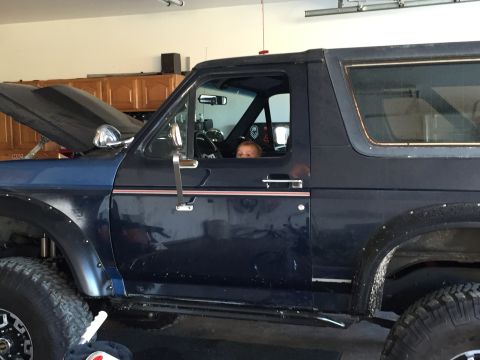 1988 Ford Bronco - A child sits in the driver's seat of a dark blue 1988 Ford Bronco parked in a garage.
