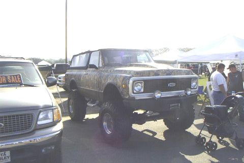 1995 Ford Bronco - This lifted 1972 Chevrolet K5 Blazer features a camouflage wrap and large off-road tires, parked next to another vehicle at an outdoor even…