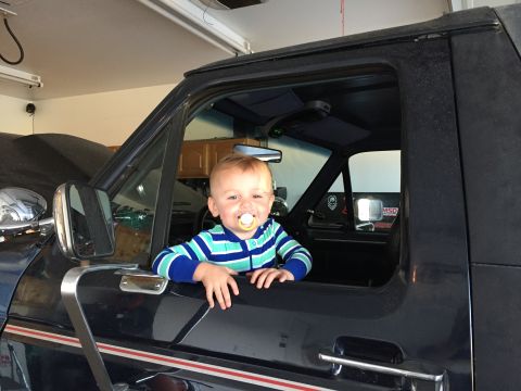 1988 Ford Bronco - Baby sits in the driver's seat of a 1988 Ford Bronco, looking out the window.