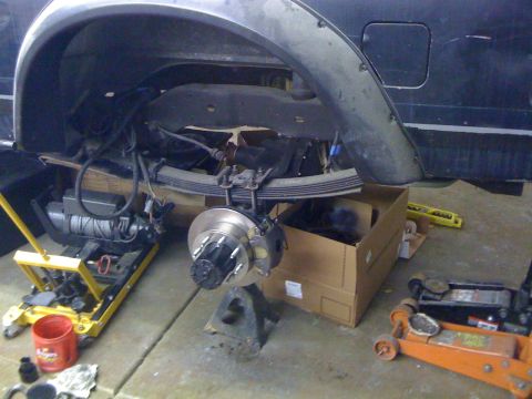 1988 Ford Bronco - The rear suspension and axle assembly of a vehicle are shown during maintenance, with tools and parts nearby.