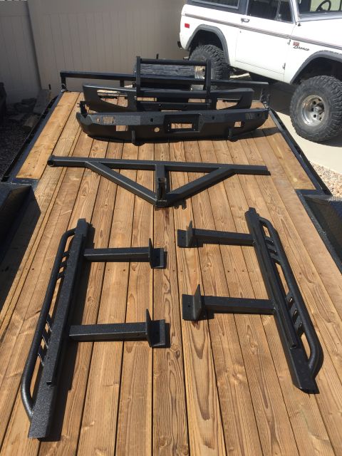 1988 Ford Bronco - Aftermarket bumpers and side steps are laid out on a wooden trailer next to a white Ford Bronco.