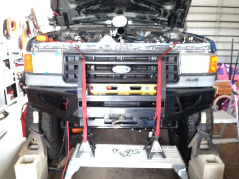 1988 Ford Bronco - Front view of a Ford truck with its hood open, a custom bumper and winch, elevated on jack stands.