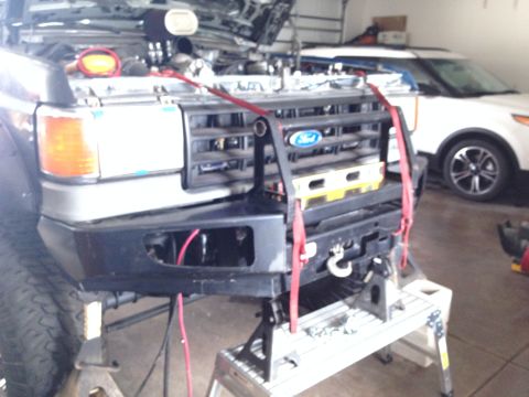 1988 Ford Bronco - The front bumper and grille of a 1988 Ford Bronco are visible while it is supported by jack stands.