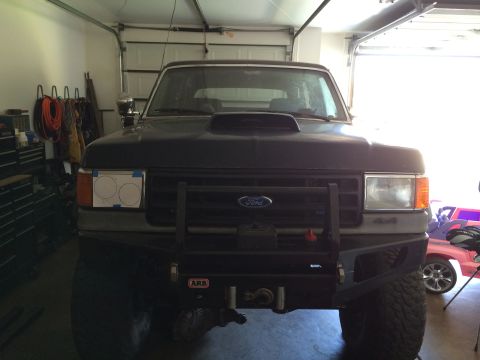 1988 Ford Bronco - Front view of a dark blue Ford Bronco with an aftermarket bumper and hood scoop, parked indoors.
