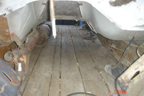 1988 Ford Bronco - Undercarriage view of a vehicle, focusing on exhaust parts and a wooden floor.