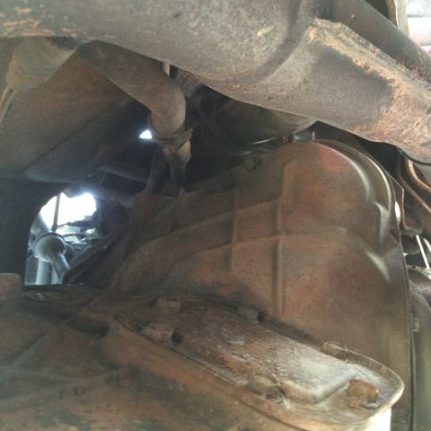 1988 Ford Bronco - Underside view of an exhaust pipe and transmission pan, with visible rust and dirt.