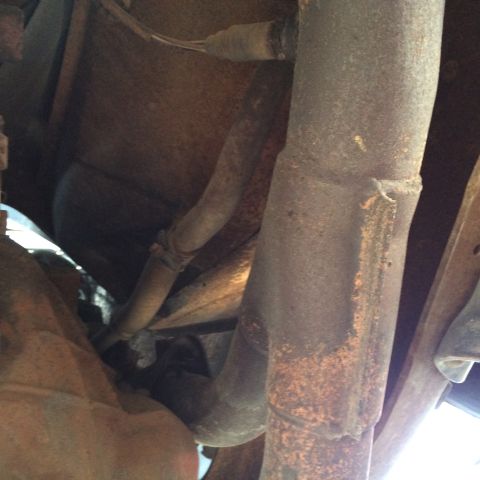 1988 Ford Bronco - Close-up view of the exhaust system and underbody of a vehicle, showing rusted metal parts.