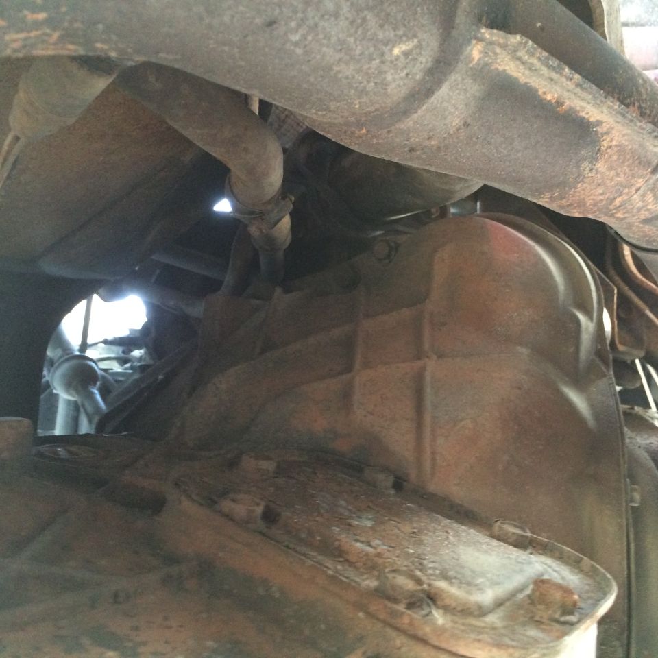 Underside view of vehicle exhaust pipe and transmission casing. Watermark reads SUPERMOTORS