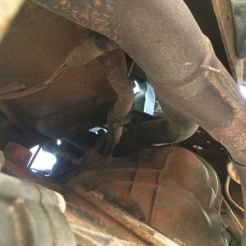 1988 Ford Bronco - Underside view of rusty exhaust pipes and a transmission housing.