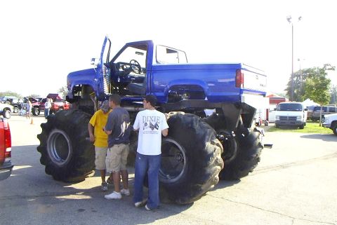 1995 Ford Bronco - A custom blue monster truck with oversized tires is parked outdoors with people standing nearby.