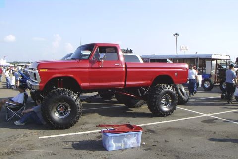 1995 Ford Bronco - A red pickup truck with a significant lift and oversized tires is parked at an outdoor event.