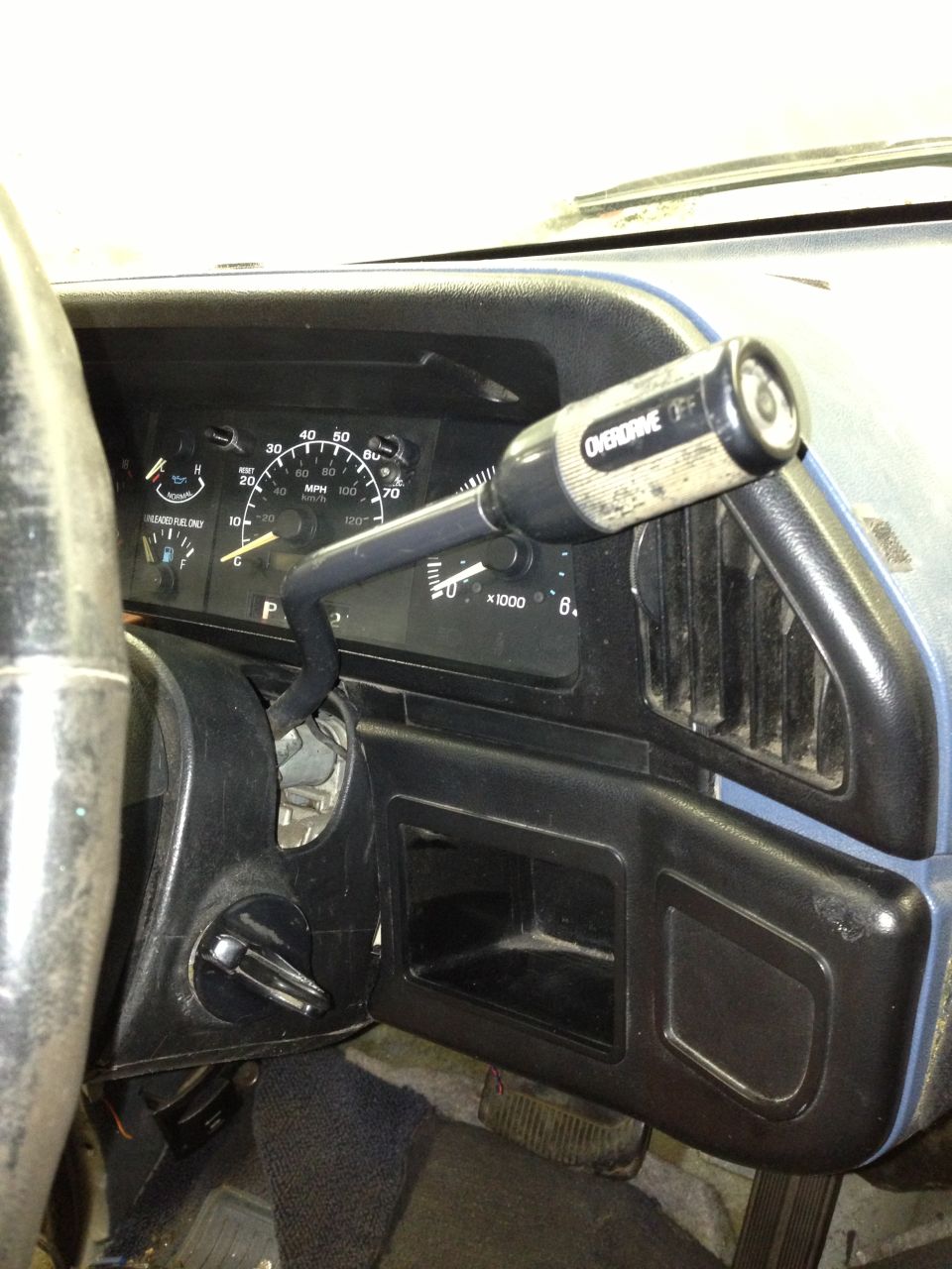 Dashboard gauges, steering wheel, and floor shifter with overdrive button. The shifter is black with a white overdrive button