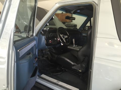 1988 Ford Bronco - Custom truck cab interior with blue lower trim, black sport seat, roll bar and shifter on display floor.