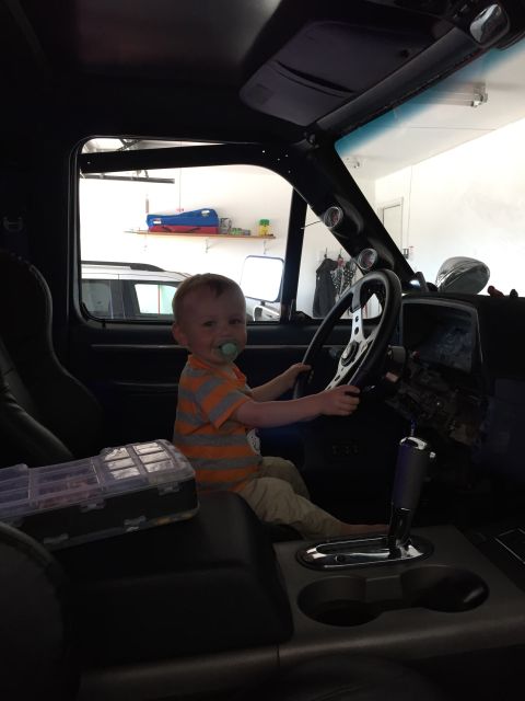 1988 Ford Bronco - A young child sits in the driver's seat of a vehicle, appearing to steer.