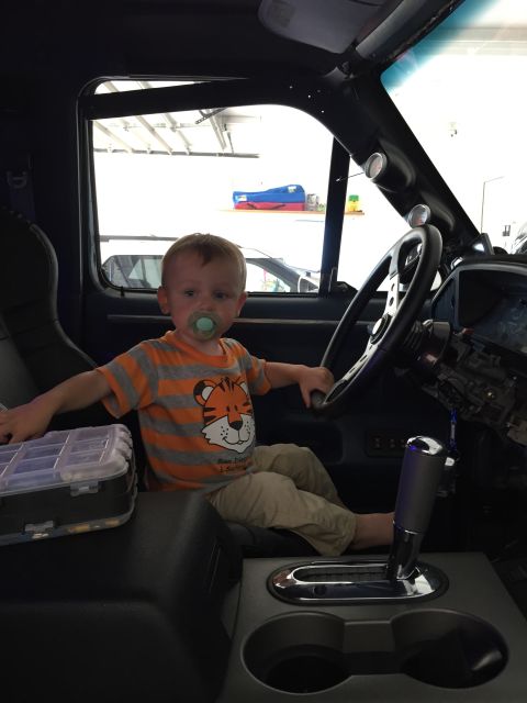 1988 Ford Bronco - young child with a pacifier sits in a truck cab, hands on the steering wheel near the console shifter.