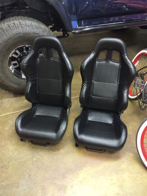 1988 Ford Bronco - Two black racing seats are displayed indoors, with a large tire and bicycle visible in the background.