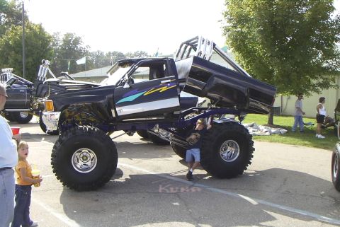 1995 Ford Bronco - A custom monster truck with large tires and a lifted body is on display at an outdoor event.