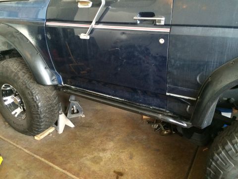 1988 Ford Bronco - The side of a dark blue 1988 Ford Bronco is shown with rock sliders installed and the vehicle supported by jack stands.