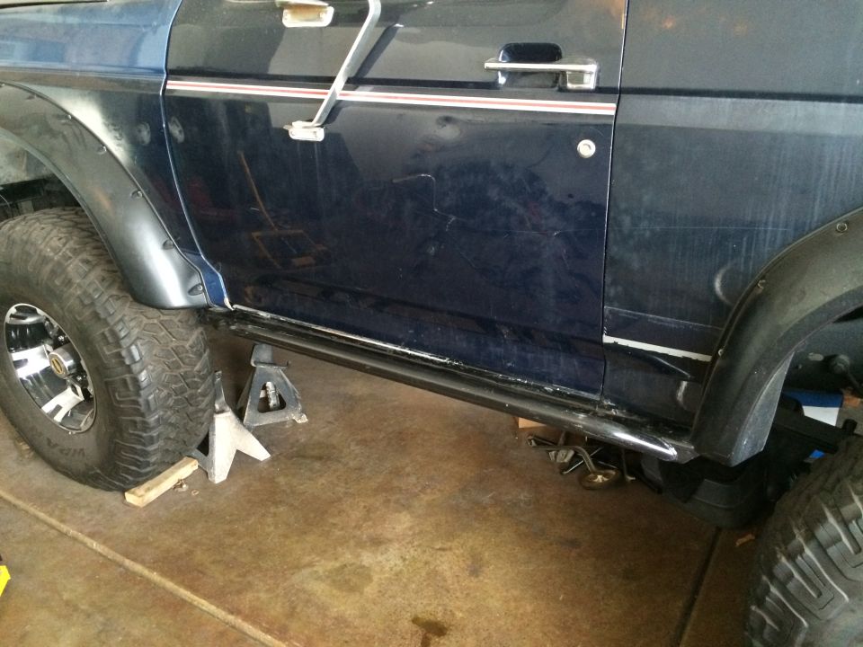 Side view of a 1988 Ford Bronco on jack stands, showing the rock sliders and large tires