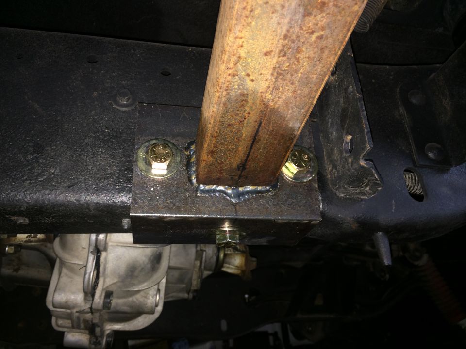 Custom welded bracket with two bolts attached to vehicle frame, near transmission