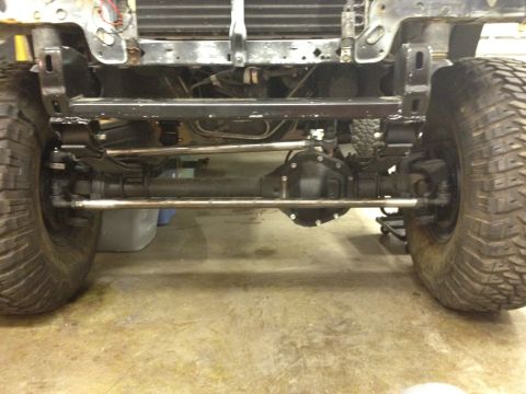 1988 Ford Bronco - The underside of a vehicle's front axle and suspension system is shown, featuring large off-road tires and aftermarket steering components.…
