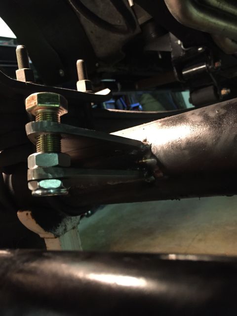 1988 Ford Bronco - A close-up view of a custom suspension modification on a vehicle, showing a metal bracket welded to a large pipe and secured with bolts and…