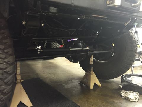 1988 Ford Bronco - The underside of a vehicle, likely a Ford Bronco, showing the front axle and steering components. The vehicle is supported by jack stands.