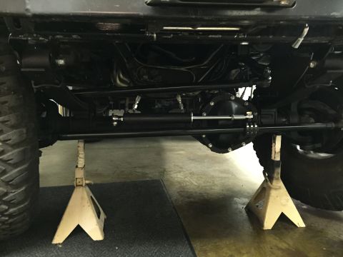 1988 Ford Bronco - The underside of a large vehicle, likely an SUV or truck, is supported by two yellow jack stands. Visible components include large tires, s…