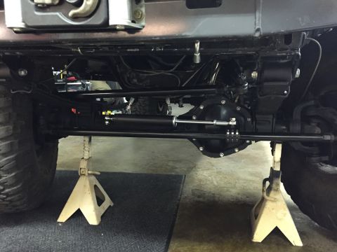 1988 Ford Bronco - The underside of a vehicle, likely a Ford Bronco, is shown supported by two jack stands. Visible components include the front axle, steerin…