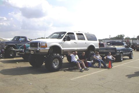 1995 Ford Bronco - A group of people relax in chairs next to a heavily modified white SUV at an outdoor event.