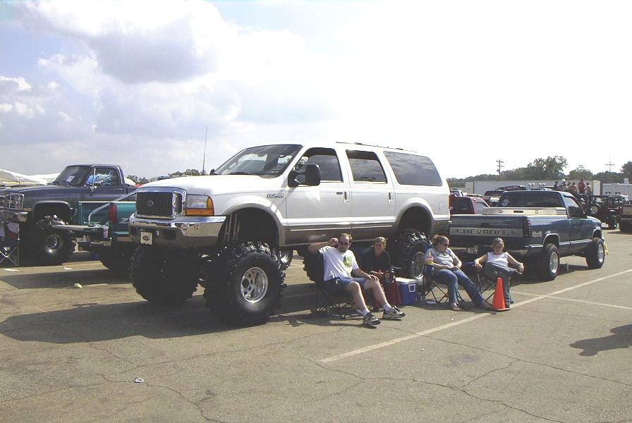 Lifted white Ford Excursion on oversized tires at a truck show with spectators