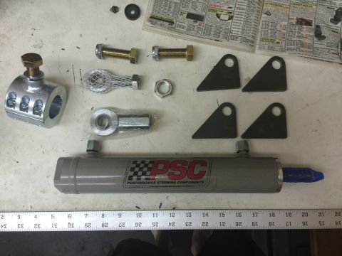 1988 Ford Bronco - A collection of steering components, including a hydraulic cylinder, tie rod ends, and mounting brackets, are laid out on a workbench next…