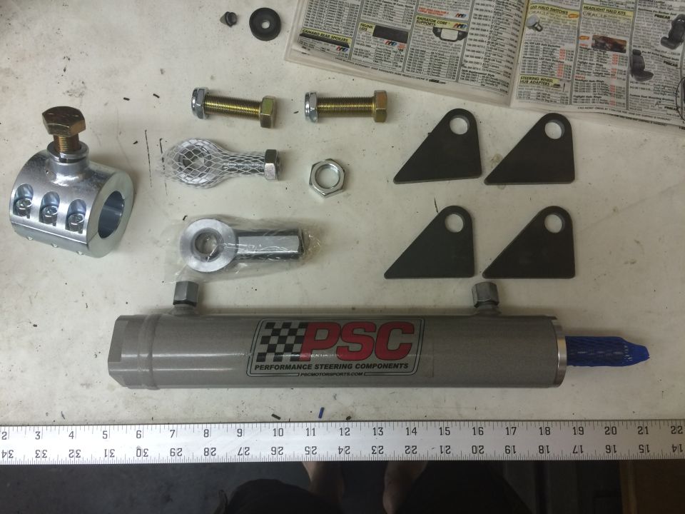 Steering components including a PSC hydraulic cylinder, tie rod ends, and brackets on a workbench.