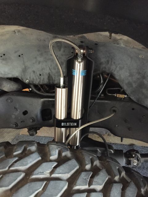 1988 Ford Bronco - A close-up view of a dual Bilstein shock absorber assembly mounted to the frame of a vehicle, with a large off-road tire in the foreground.