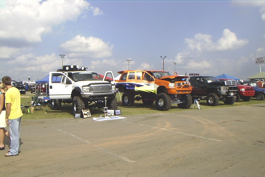 Row of lifted show trucks on grass at an outdoor truck show