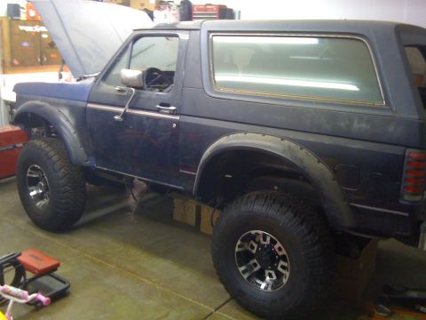 1988 Ford Bronco - A dark blue Ford Bronco is parked in a garage with its hood up. The vehicle has large off-road tires and fender flares, suggesting modifica…