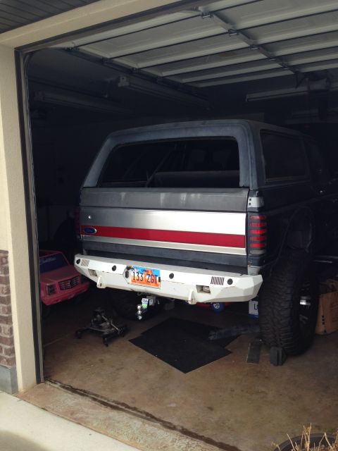 1988 Ford Bronco - The rear of a dark blue and silver Ford Bronco is parked in a garage. It has a white aftermarket bumper with a Utah license plate reading "…