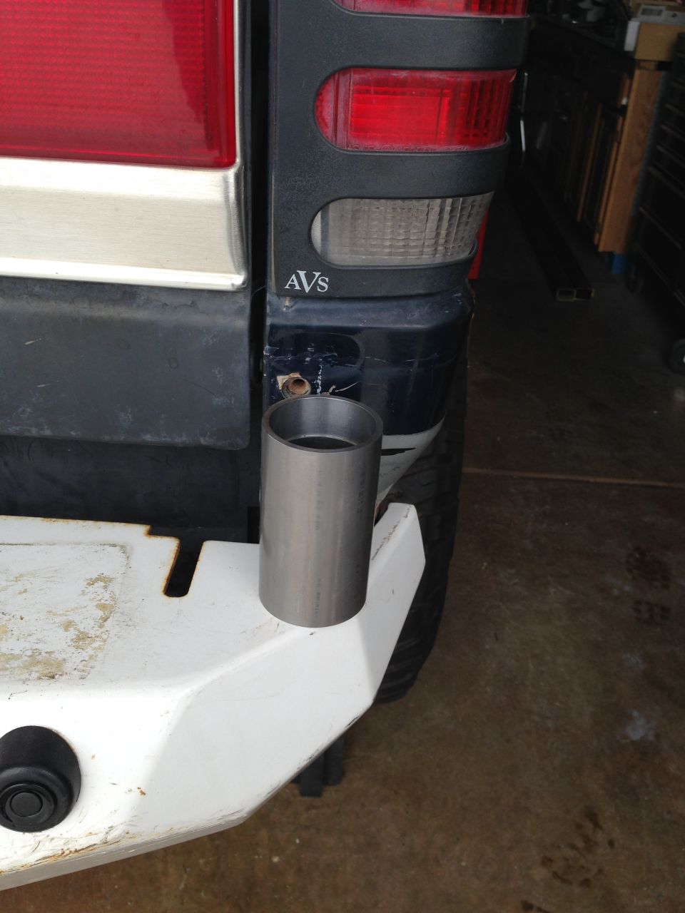 Rear corner of a dark blue SUV with a silver tube on a white bumper.