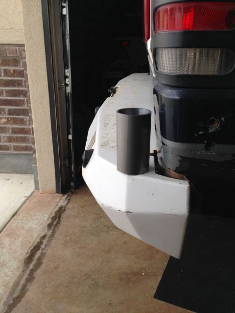 1988 Ford Bronco - A dark gray cylindrical part is resting on the corner of a white aftermarket bumper, attached to the rear of a dark blue vehicle. The vehic…