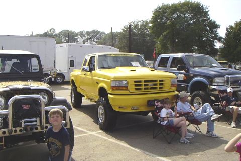 1995 Ford Bronco - A yellow Ford F-Series pickup truck is parked at an outdoor event with other vehicles and spectators.