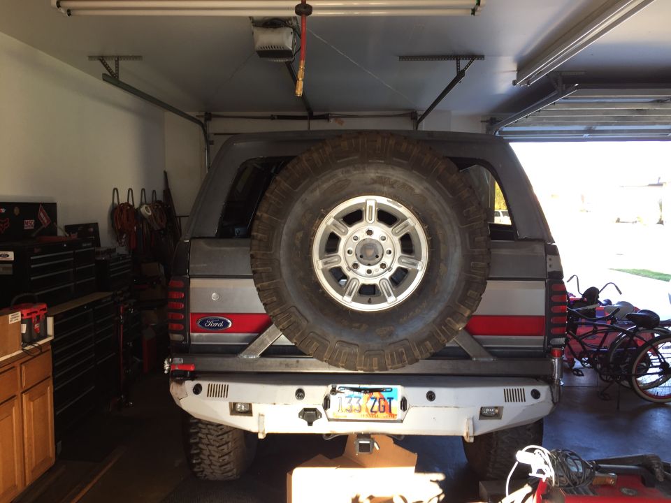 1988 Ford Bronco rear view with spare tire, custom bumper, and license plate in a garage.