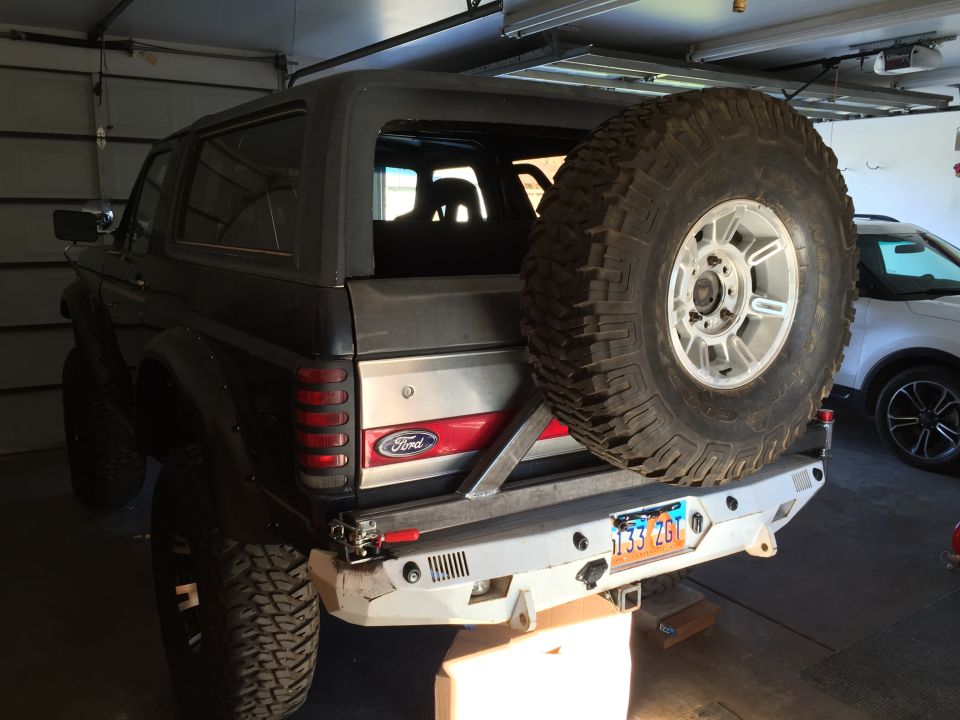 Rear view of a lifted dark Ford Bronco with a spare tire on the back and custom bumper.